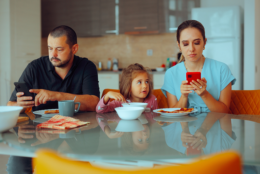 parents sitting with their child but they're using their phones