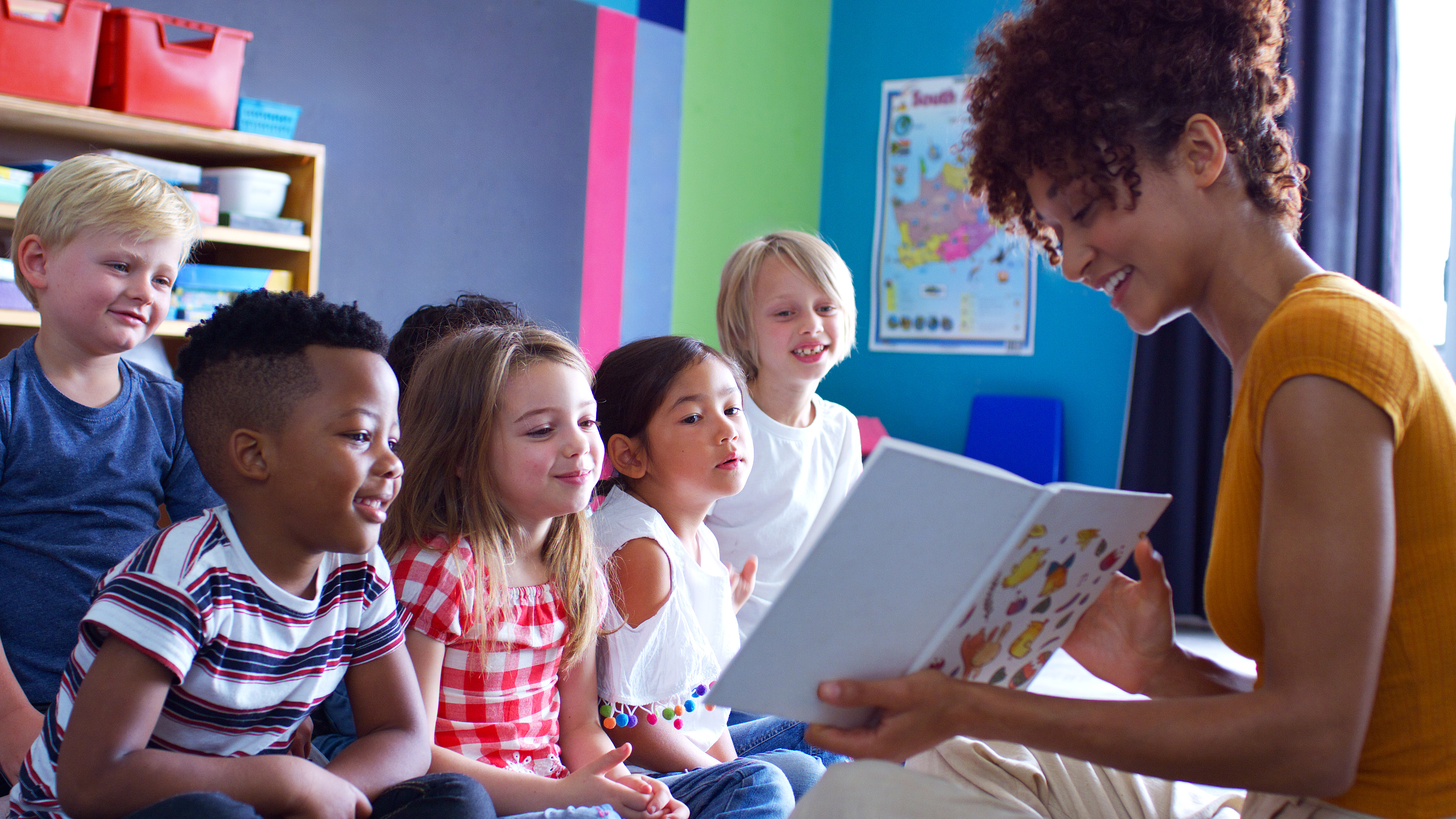 educator sitting on the floor and reading to a group of happy young children